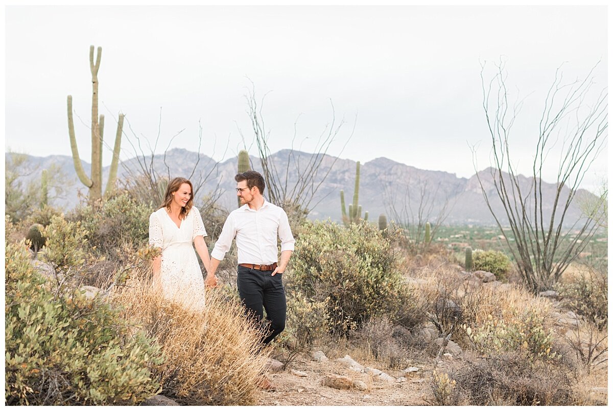 Desert engagement session with couple walking hand in hand with saguaros and desert landscape