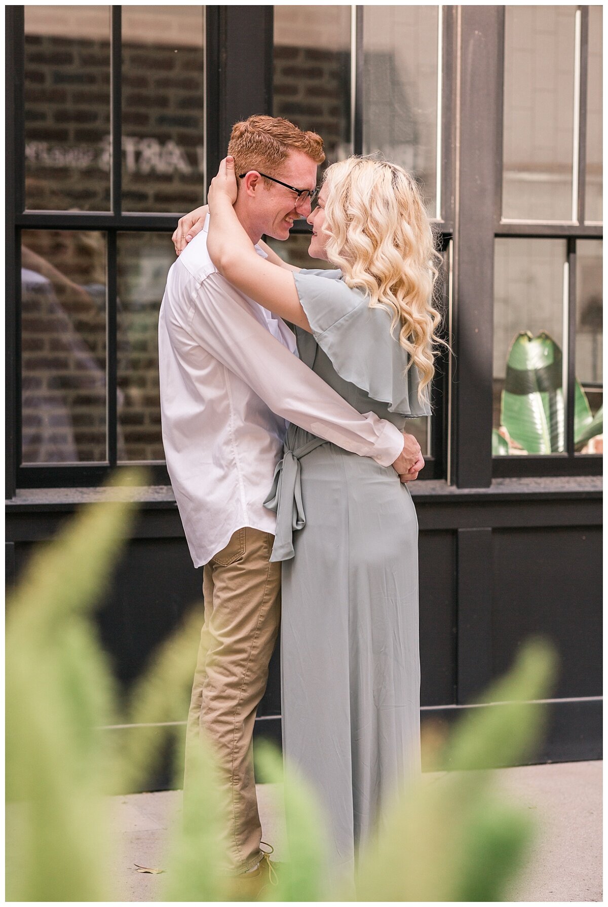 Engagement pictures at St. Phillips Plaza in Tucson, Arizona. Couple wearing grey maxi dress and white shirt with tan pants. Couple holds each other close, nose to nose, while Melissa Fritzsche Photography captures the sweet moment.