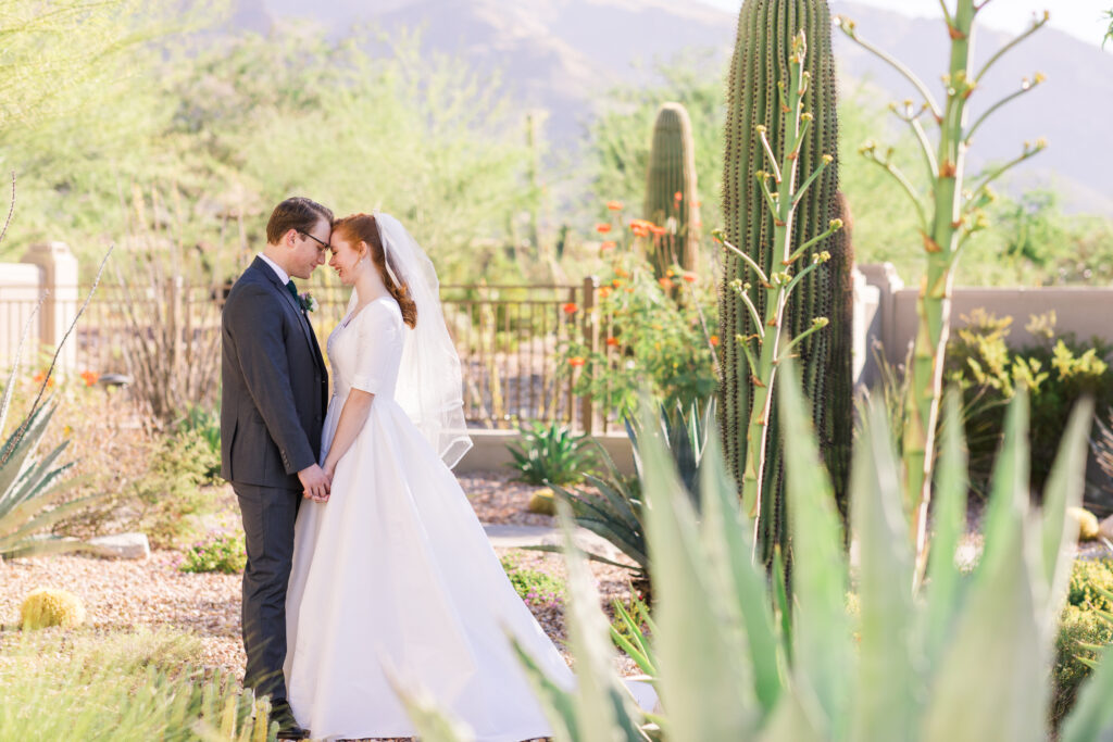 Bride and Groom leaning head together on their wedding day with saguaros and agave cacti surrounding them.