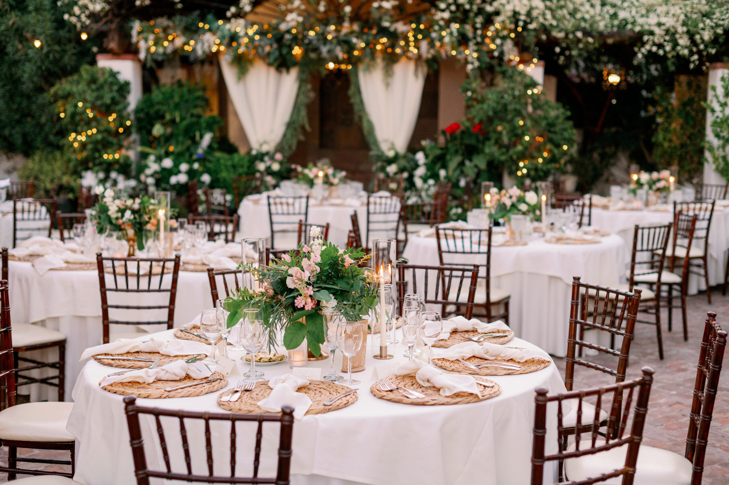 Stillwell House wedding reception courtyard with pink floral centerpieces, romantic draping, and the lush greenery ceremony area in the background.